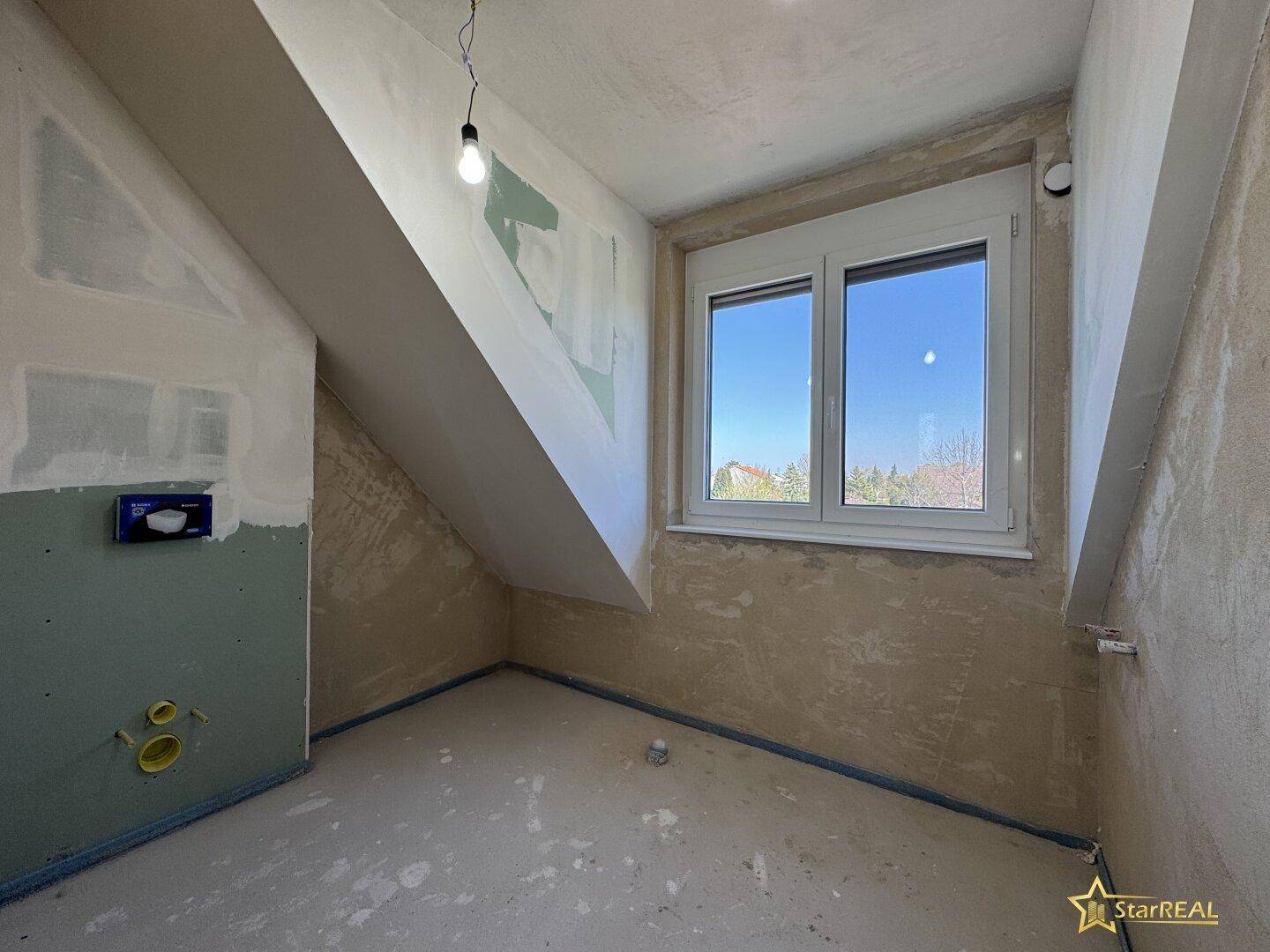 Unfertiges Badezimmer im Dachgeschoss mit Schrägen und Rohinstallationen.