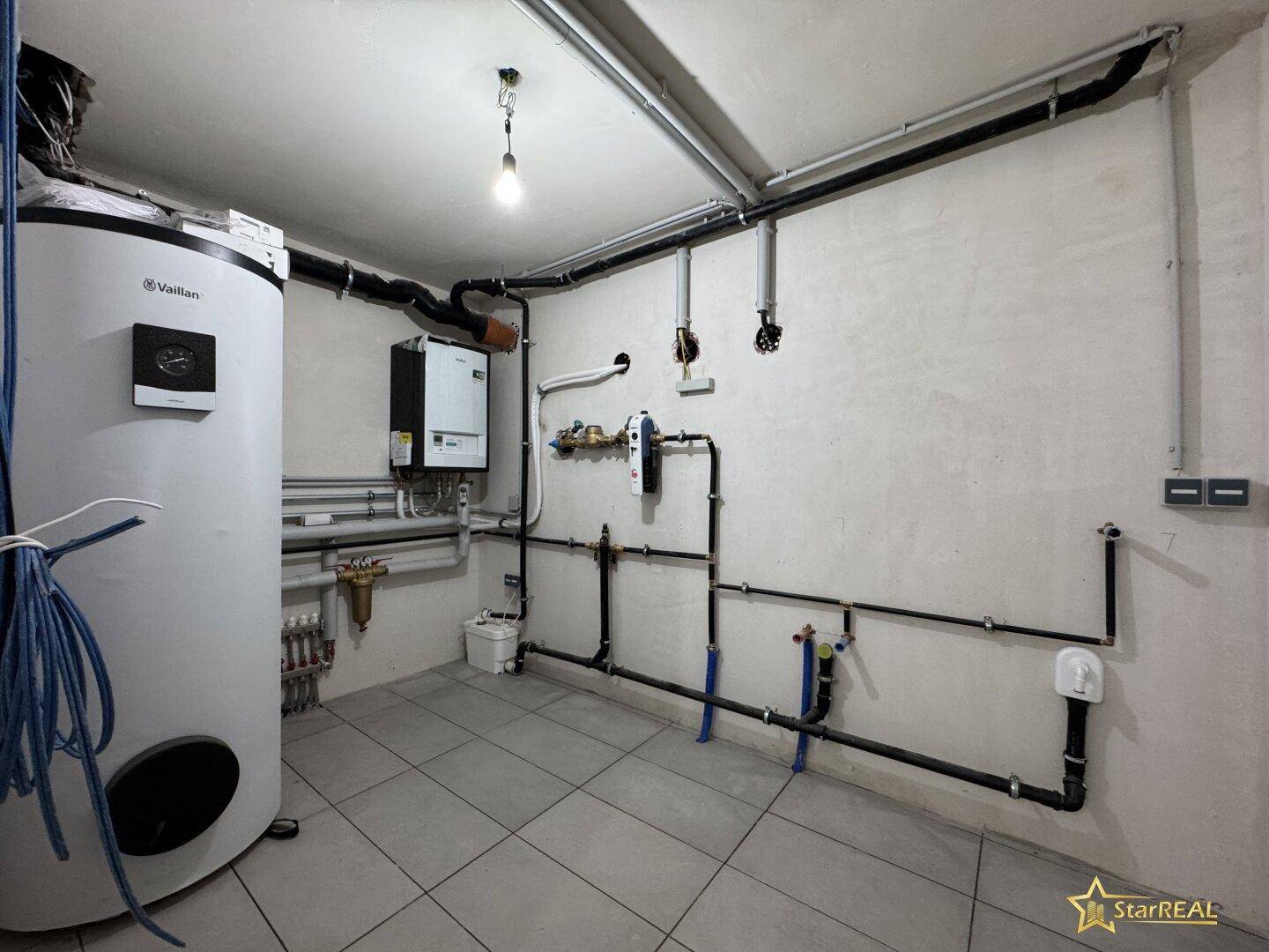 Technikraum mit Warmwasserspeicher, Heizungsanlage und sichtbaren Rohrleitungen.