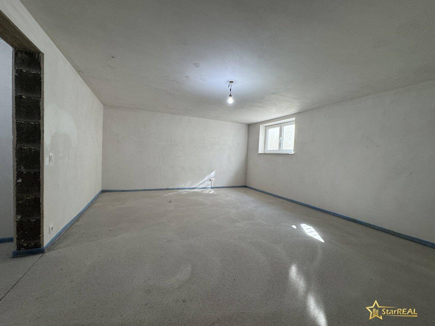 Unfertiger Kellerraum mit kleinem Fenster und Betonboden, ideal als Abstellraum.