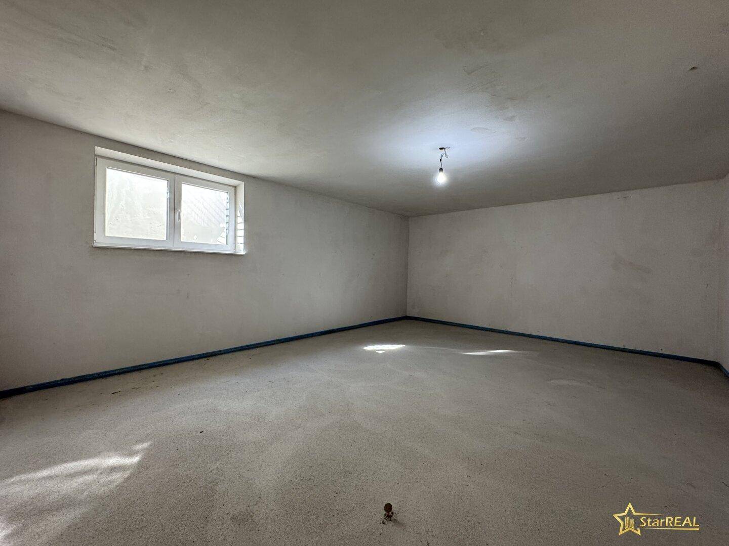Geräumiger, unfertiger Kellerraum mit Fenster und Betonboden, bereit für den Ausbau.