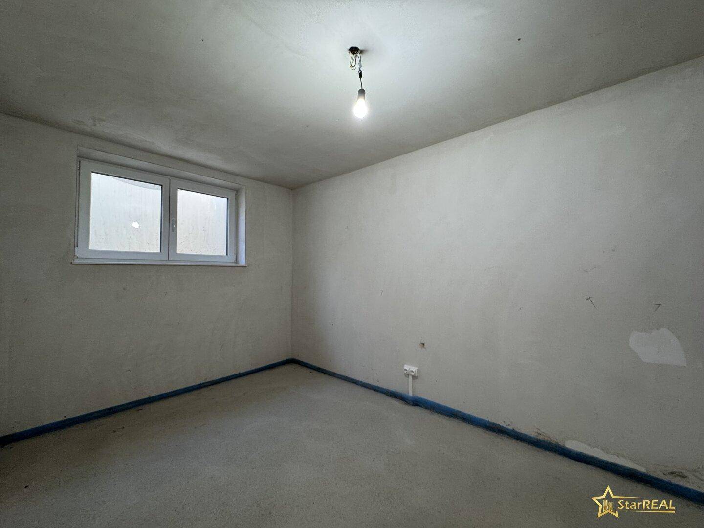 Unfertiger Kellerraum mit kleinem Fenster und Betonboden, der auf den Ausbau wartet.