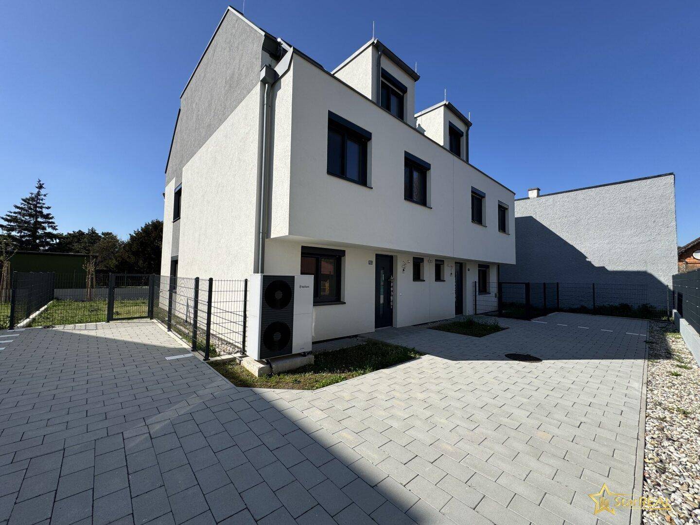 Moderne Neubaufassade mit gepflasterter Einfahrt und installierter Wärmepumpe.