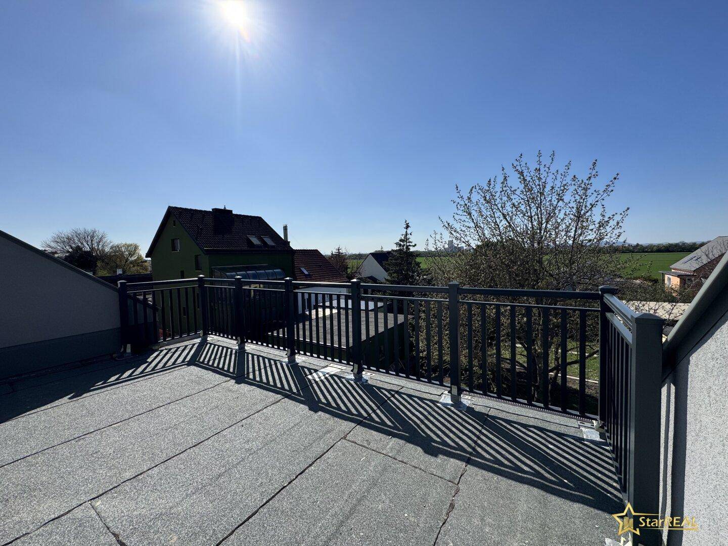 Sonniger Blick von der unfertigen Dachterrasse auf die umliegende Landschaft und Häuser.