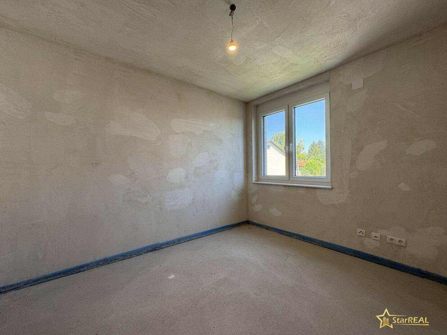 Helles, unfertiges Schlafzimmer mit Fenster und Rohbauwänden, bereit für den Innenausbau.