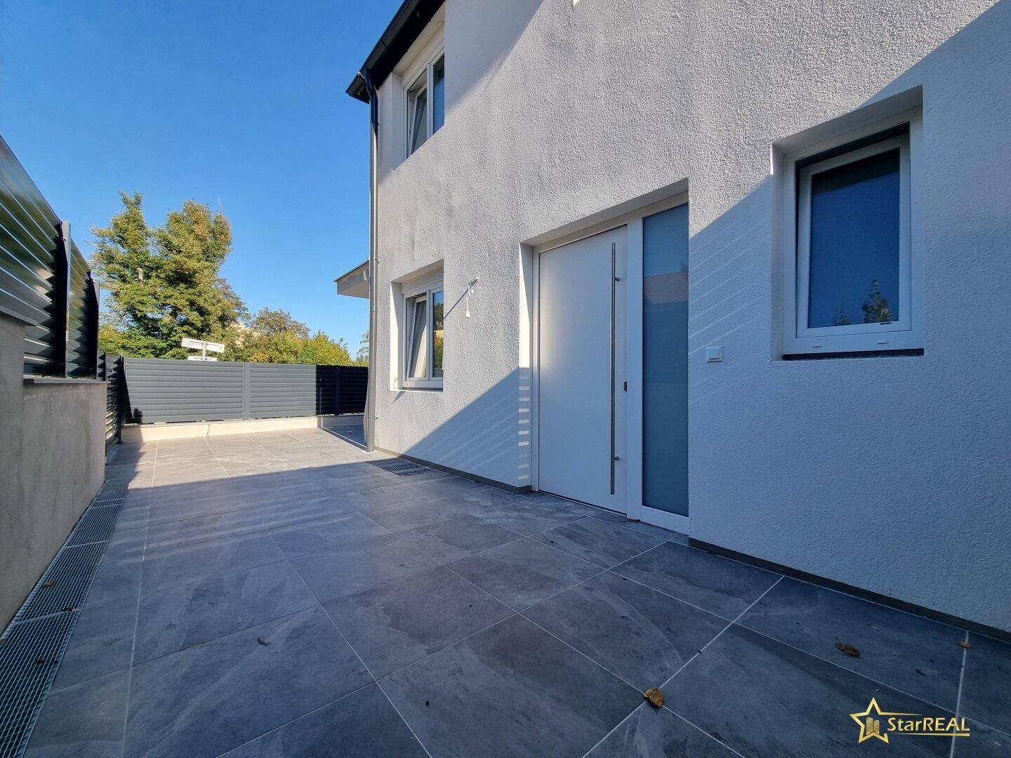 Heller Eingangsbereich mit moderner Haustür und großformatigen Fliesen im Außenbereich.