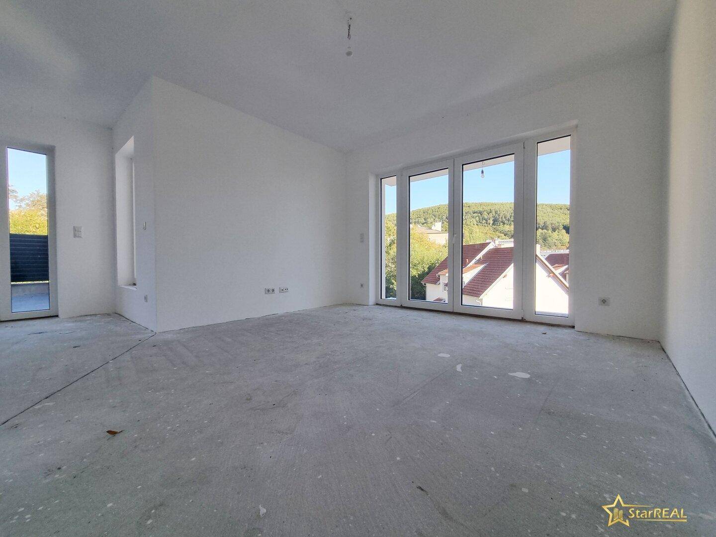 Lichtdurchfluteter Raum im Rohbau mit großen Fenstern und Blick auf die Umgebung.