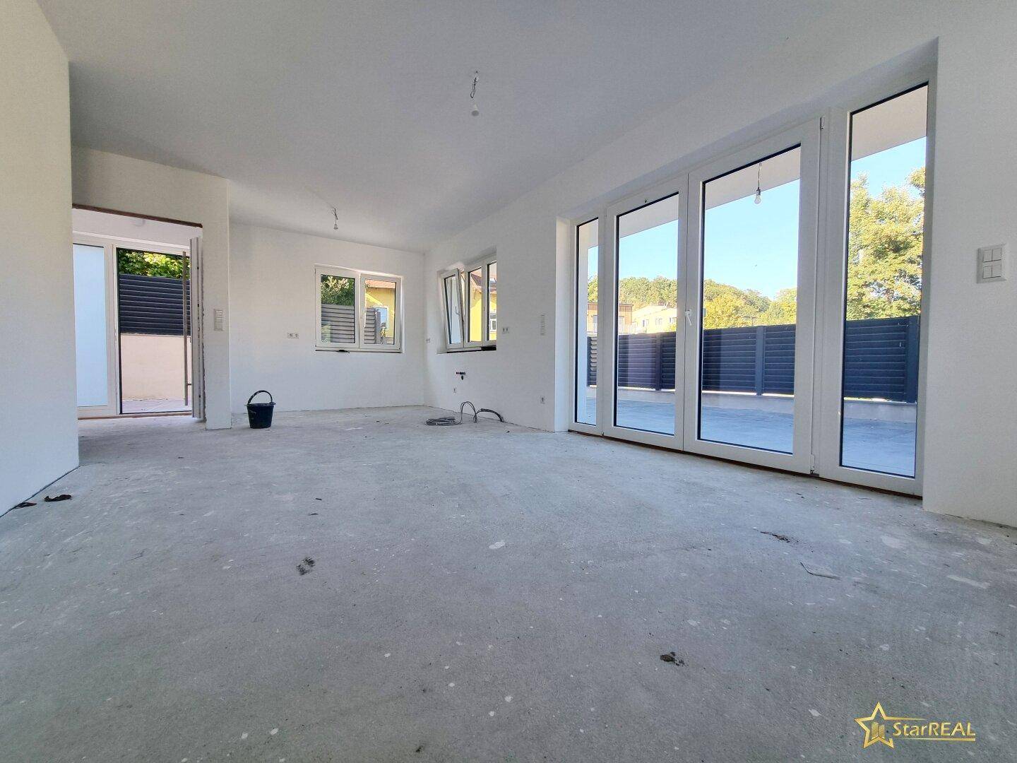 Heller Wohnbereich im Rohbau mit großen Fenstern und Zugang zur Außenterrasse.