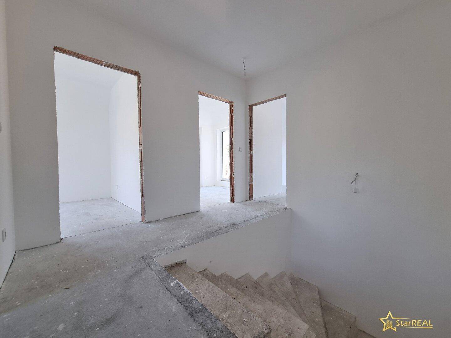 Treppenaufgang und Flurbereich im Rohbau mit Zugang zu weiteren Räumen.