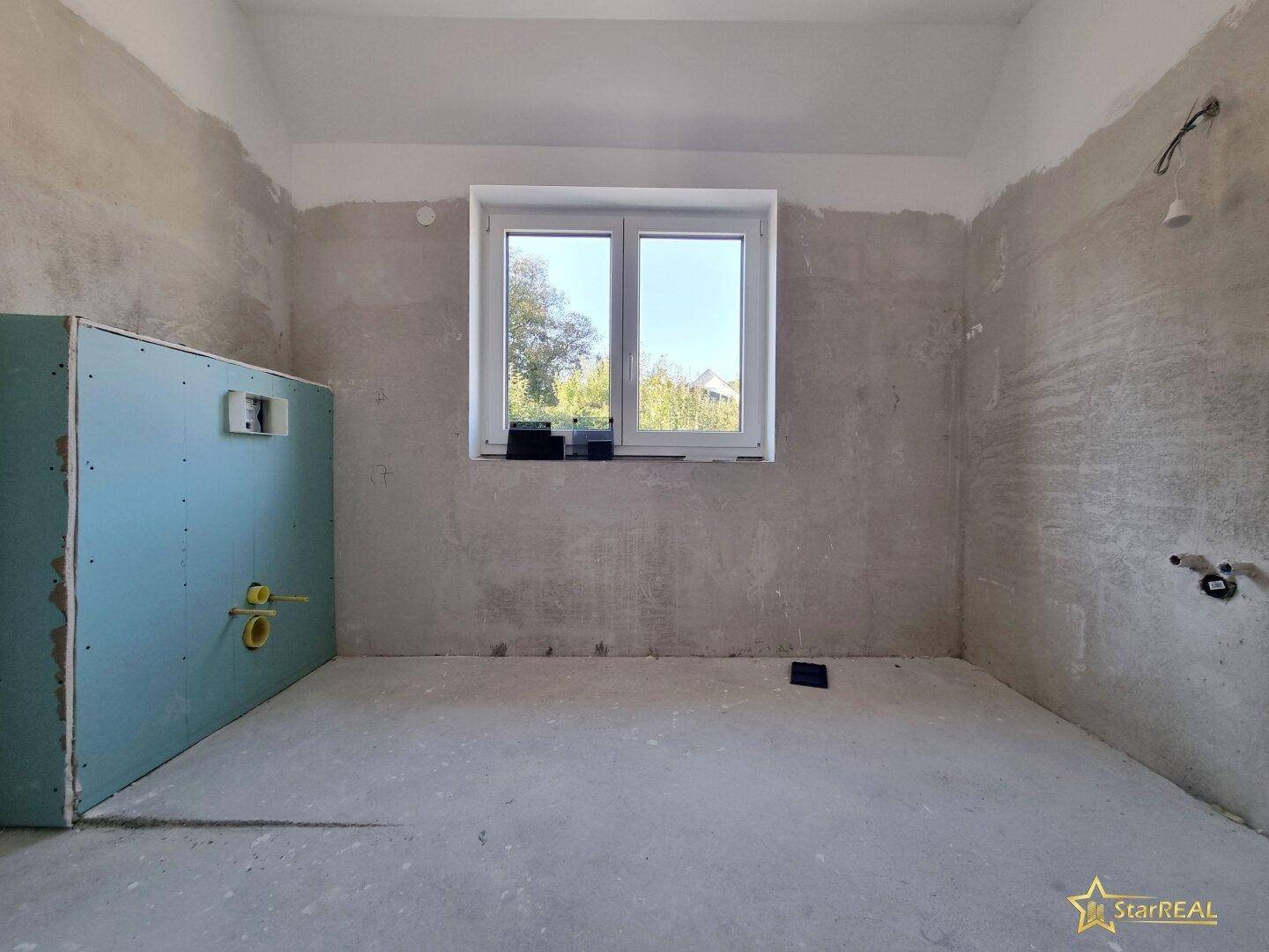 Badezimmer im Rohbauzustand mit Fenster und vorbereiteten Anschlüssen.