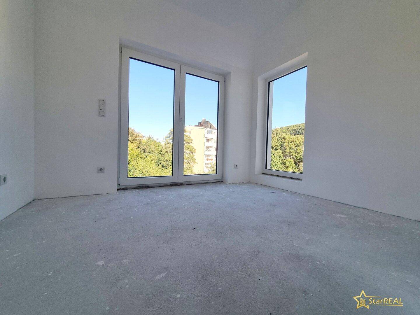 Heller Raum im Rohbau mit großen Fenstern und Blick auf die umliegende Bebauung.