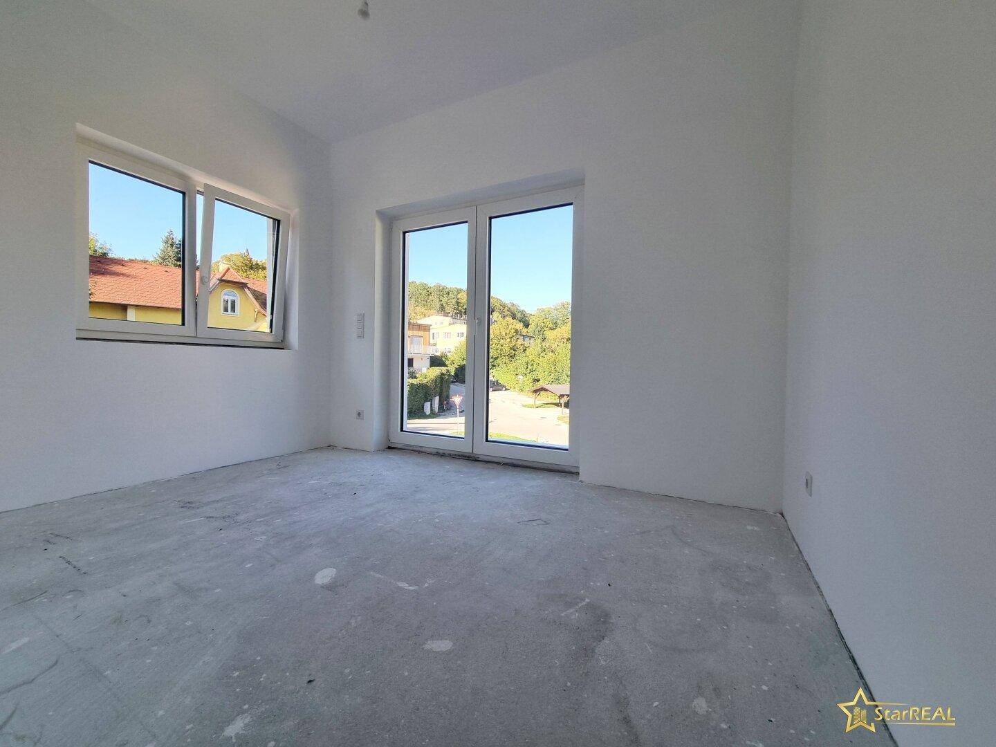 Raum im Rohbau mit viel Tageslicht und Zugang zu einem Außenbereich.