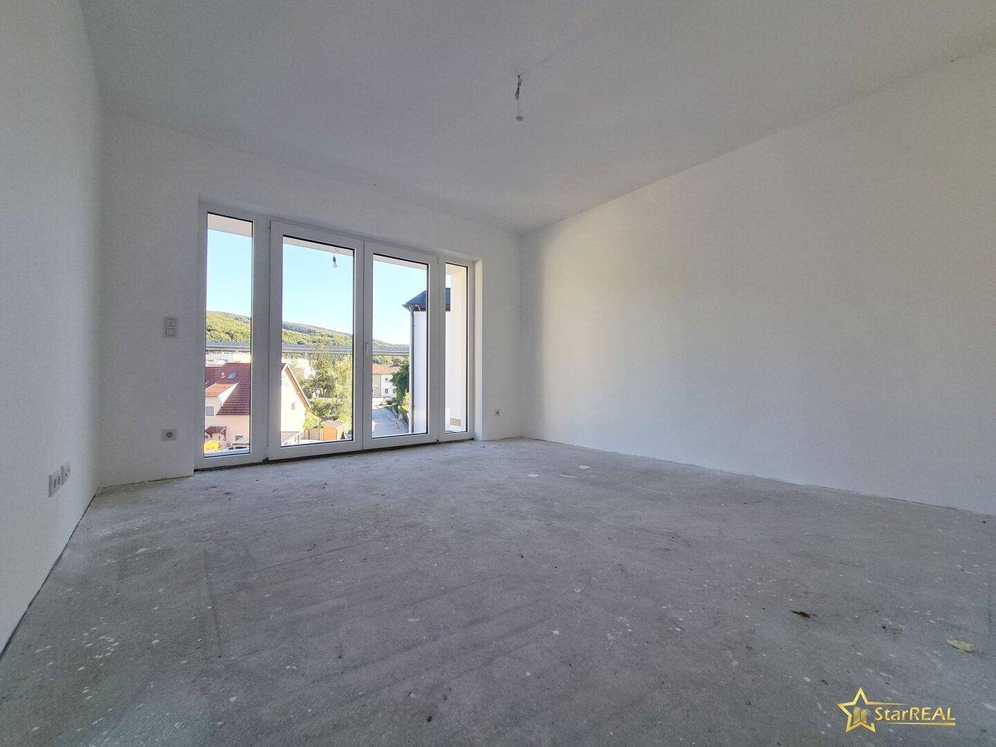 Heller Raum im Rohbau mit großen Fenstern, die viel Licht hereinlassen.