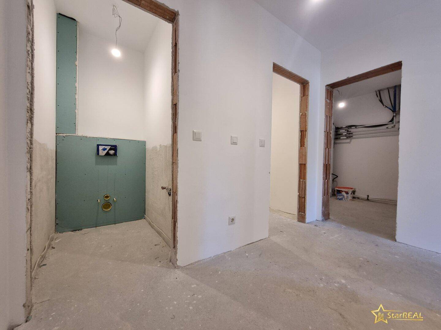 Flurbereich im Rohbau mit vorbereitetem Badbereich und weiteren Türöffnungen.