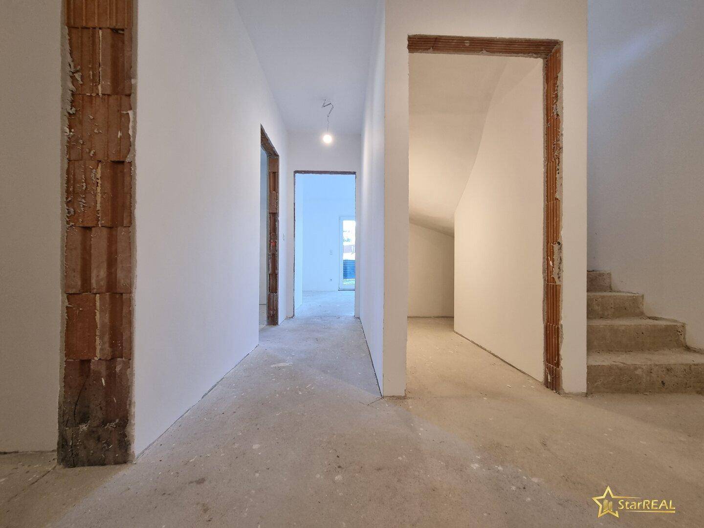 Flurbereich im Rohbau mit sichtbaren Ziegelwänden und Treppenaufgang.