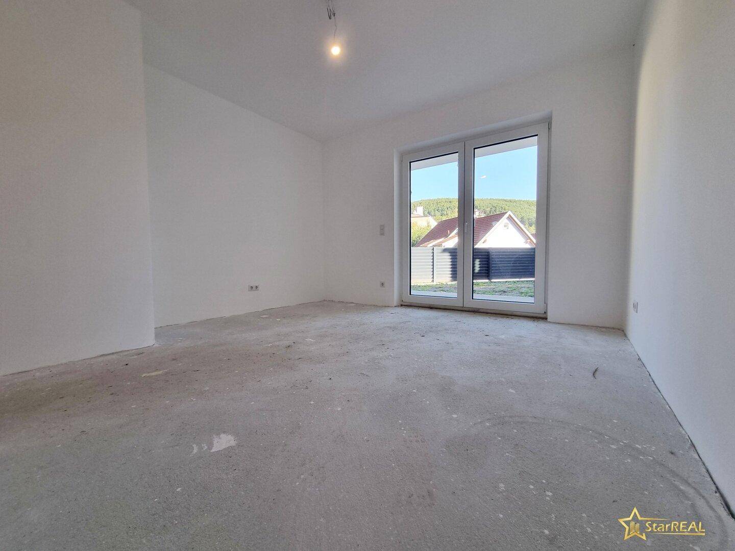 Heller Raum im Rohbau mit Zugang zu einem Außenbereich und Blick ins Grüne.