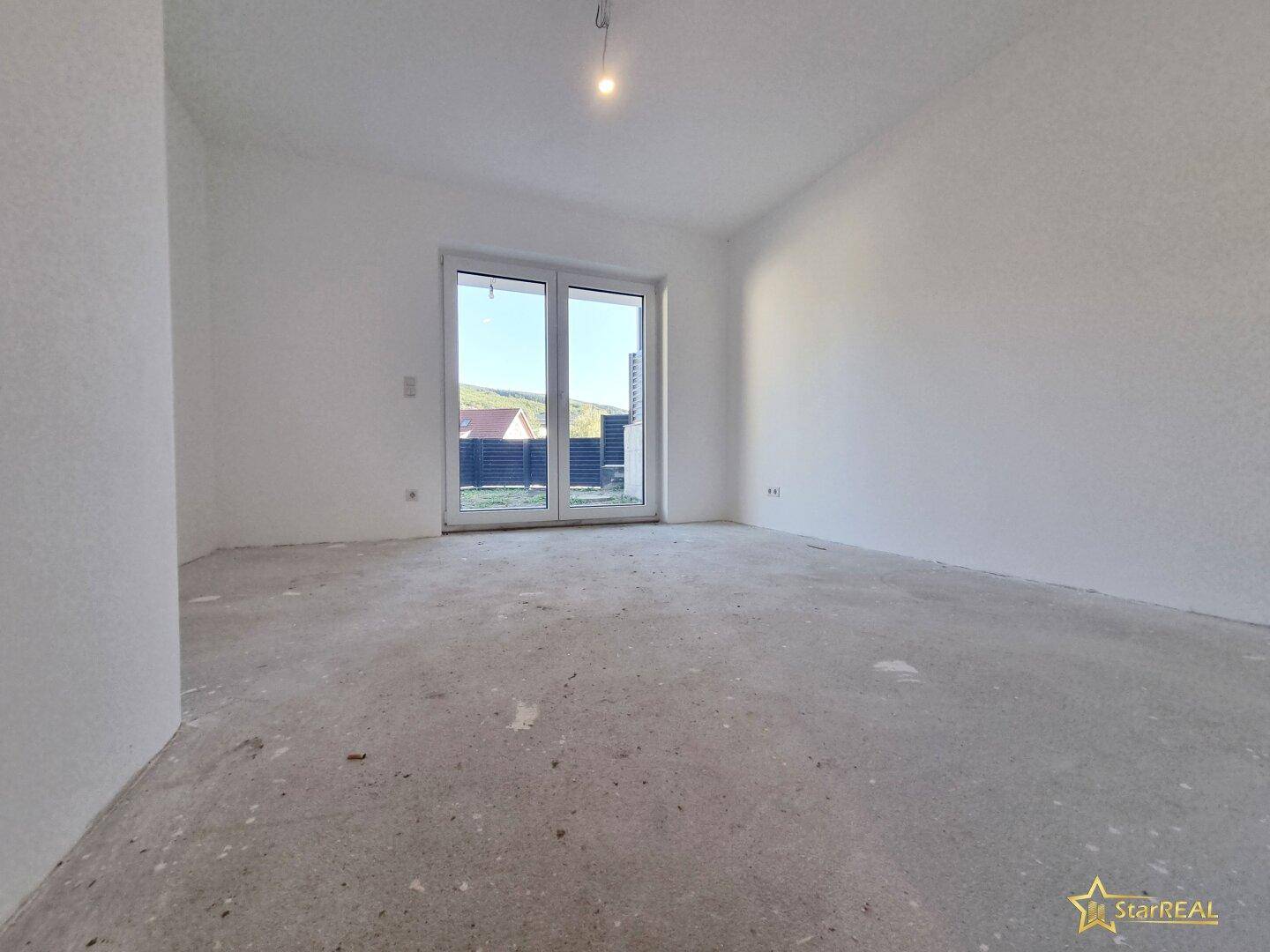 Raum im Rohbau mit viel Tageslicht und Zugang zu einem Außenbereich.