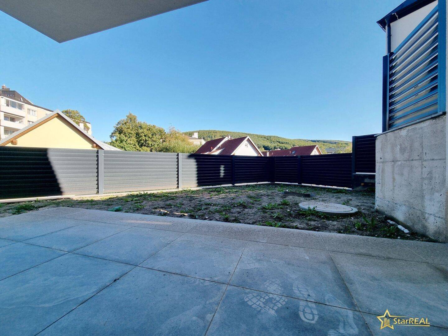 Gartenbereich mit Rasen und einer gepflasterten Terrasse, umgeben von einem Zaun.