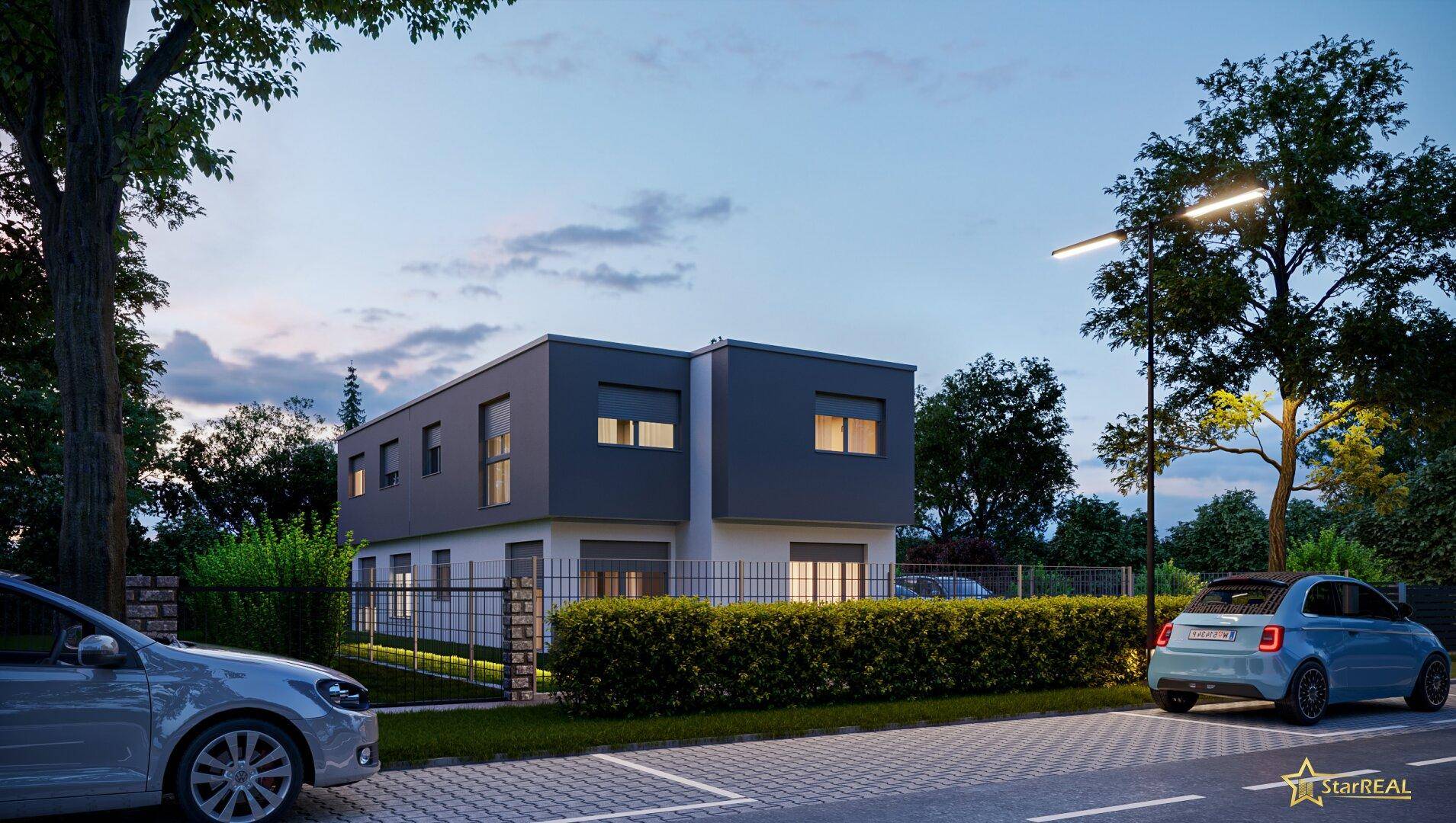 Modernes Gebäude bei Dämmerung mit beleuchteter Fassade und gepflegter Hecke entlang der Straße.