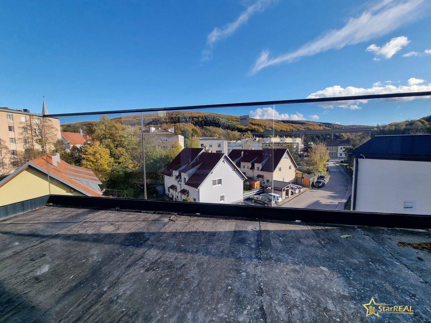 Weitblick über die umliegende Wohngegend und grüne Hügel von einem Balkon.