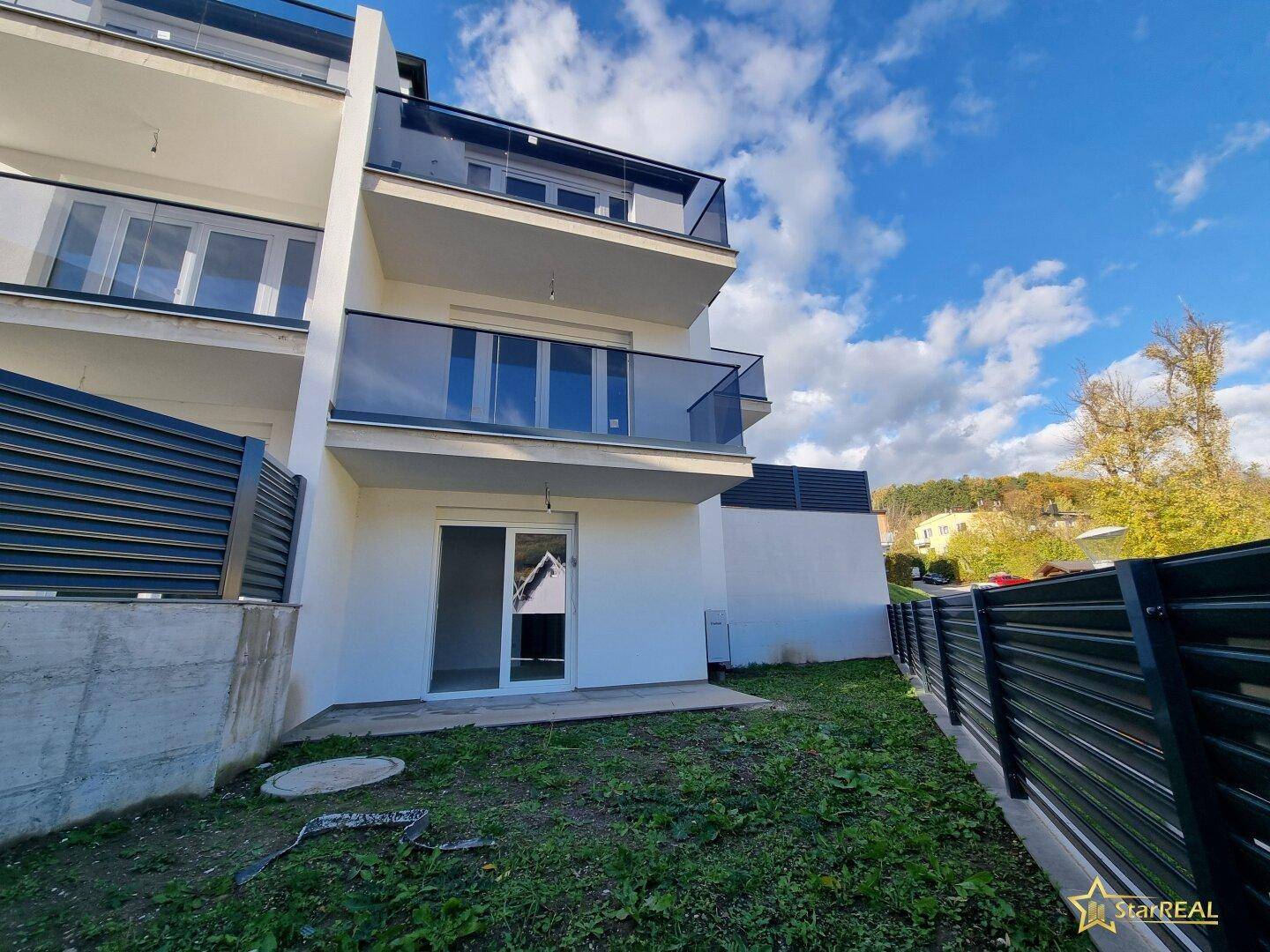 Moderne Gebäudefassade mit Balkonen und einem kleinen Gartenbereich im Erdgeschoss.