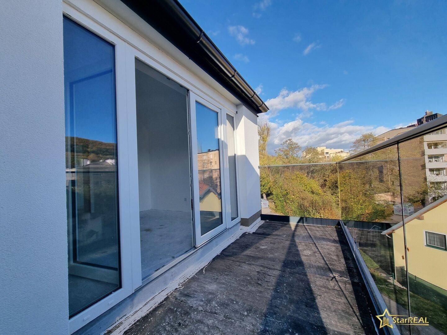 Balkon mit Glasgeländer und weitem Blick über die Dächer der Nachbarschaft.
