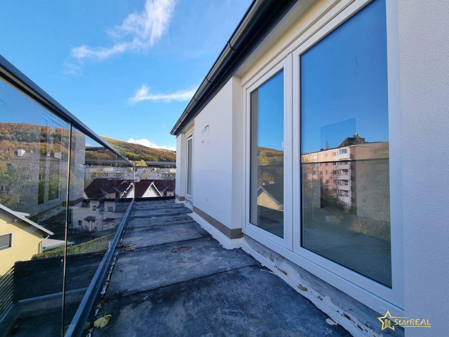 Balkon mit Glasgeländer und Blick auf die umliegende Wohnbebauung und Natur.