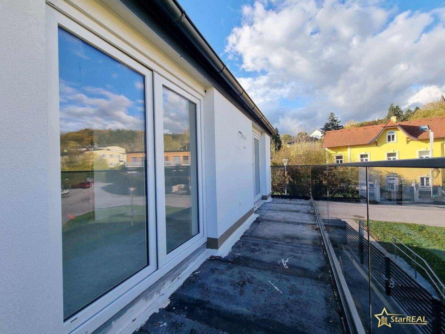 Balkon mit Glasgeländer und Blick auf die Straße und die umliegende Natur.