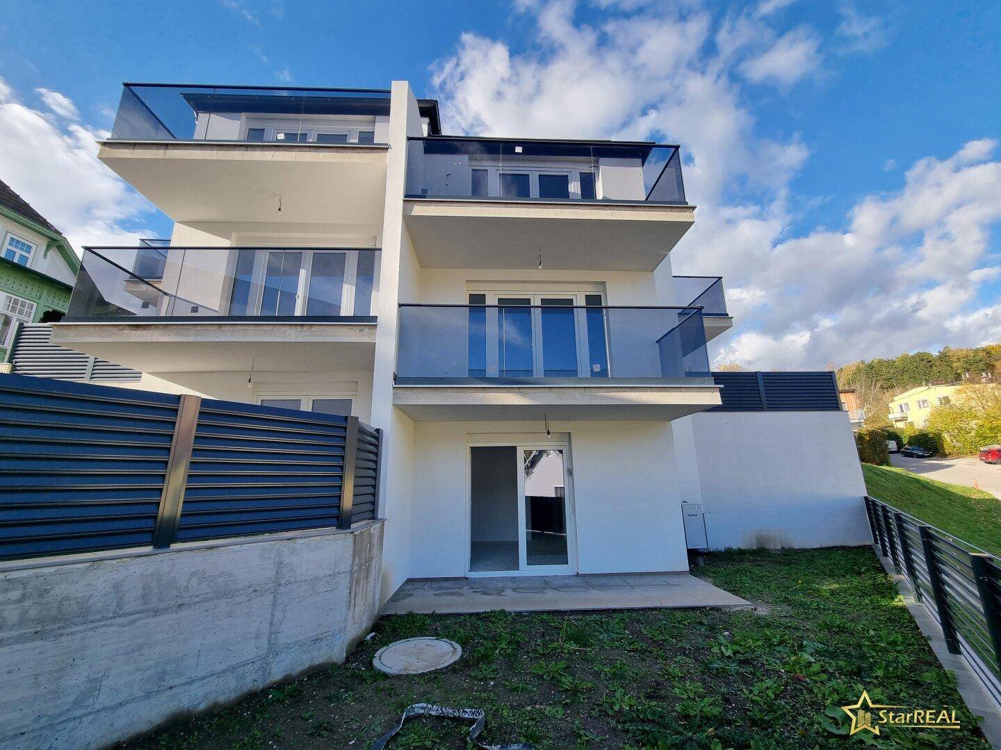 Moderne Gebäudefassade mit Balkonen und einem kleinen Gartenbereich im Erdgeschoss.