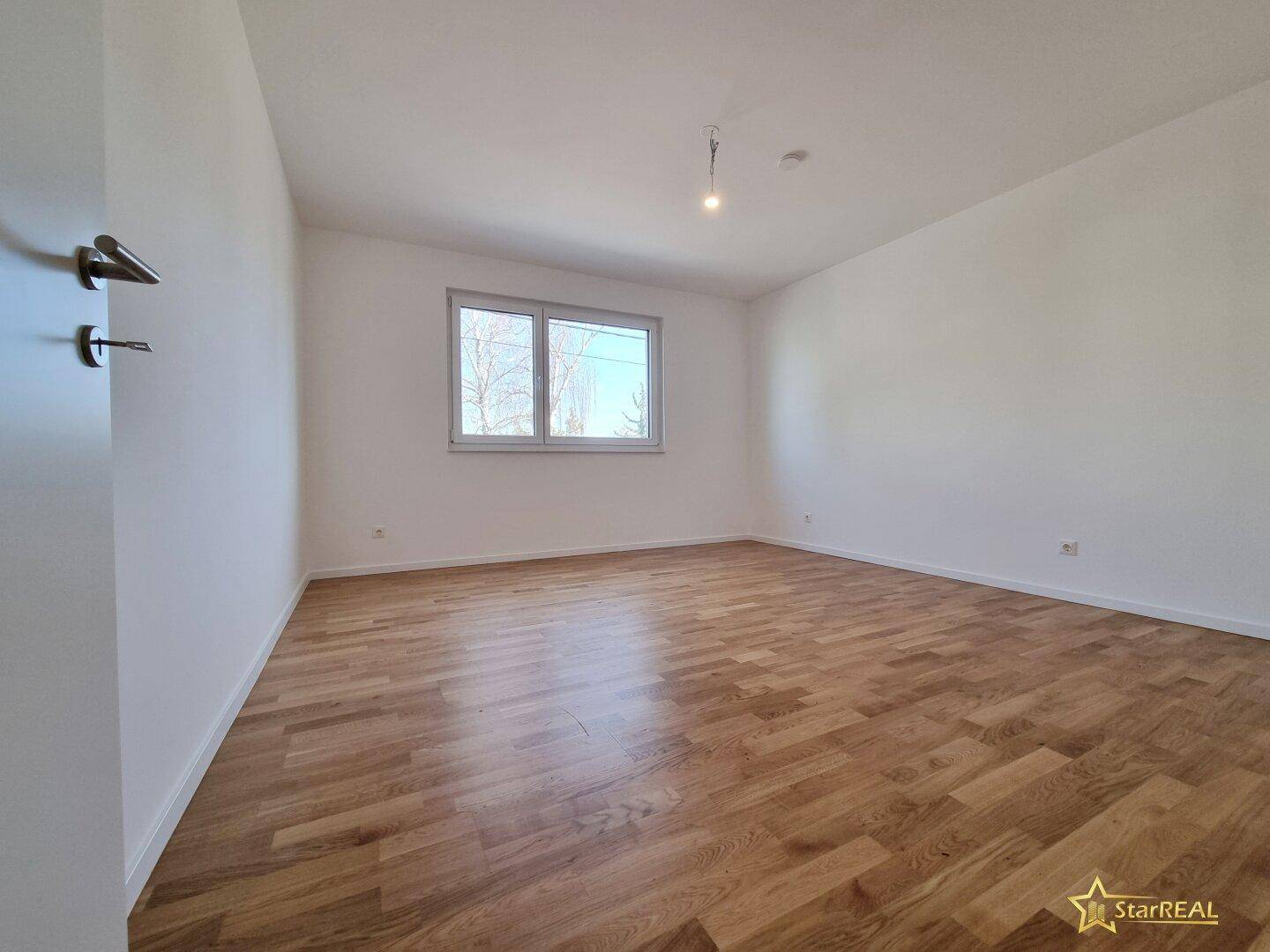 Helles Schlafzimmer mit Parkettboden, weißen Wänden und einem Fenster.