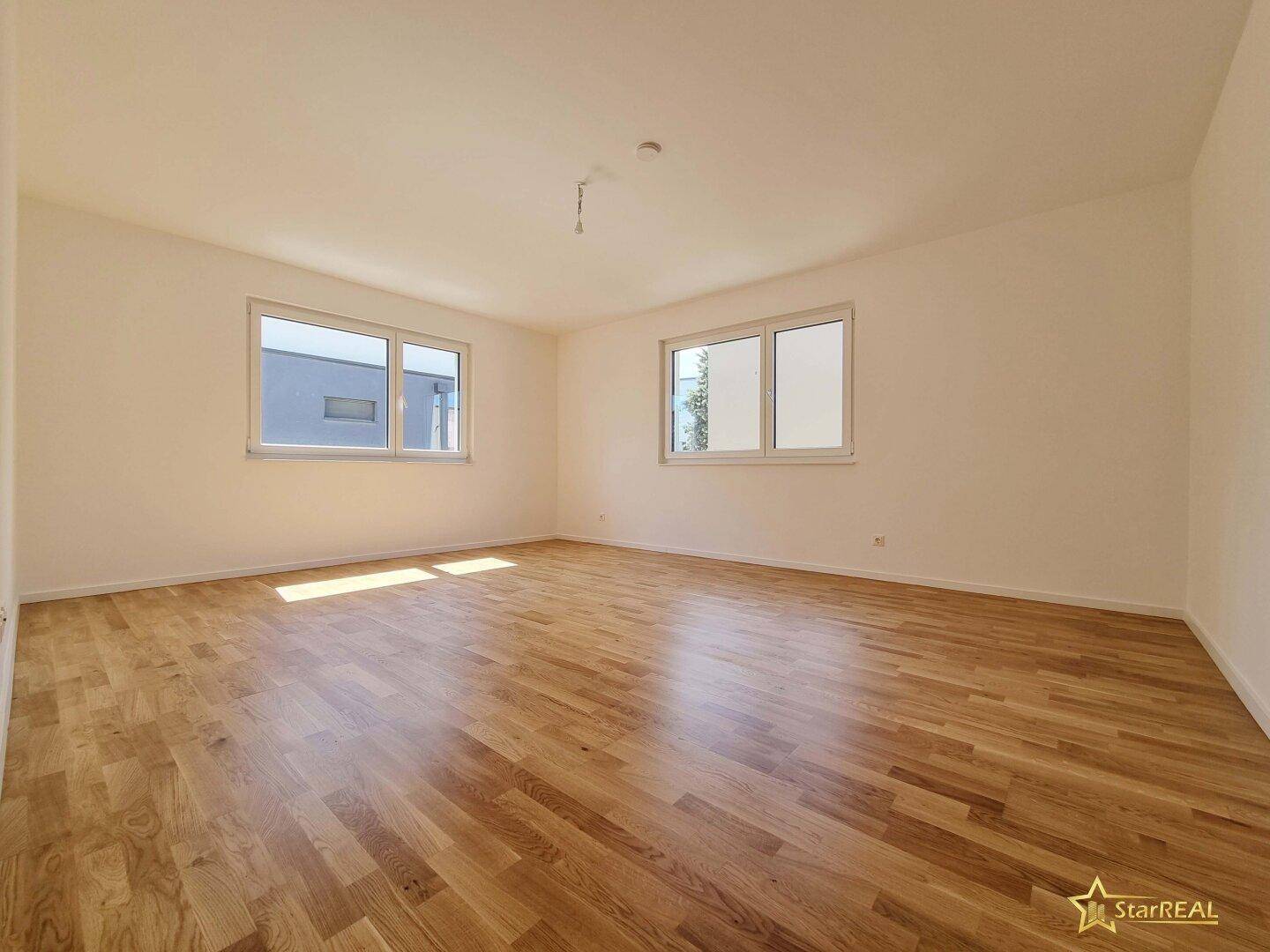 Helles Schlafzimmer mit Parkettboden, weißen Wänden und zwei Fenstern.