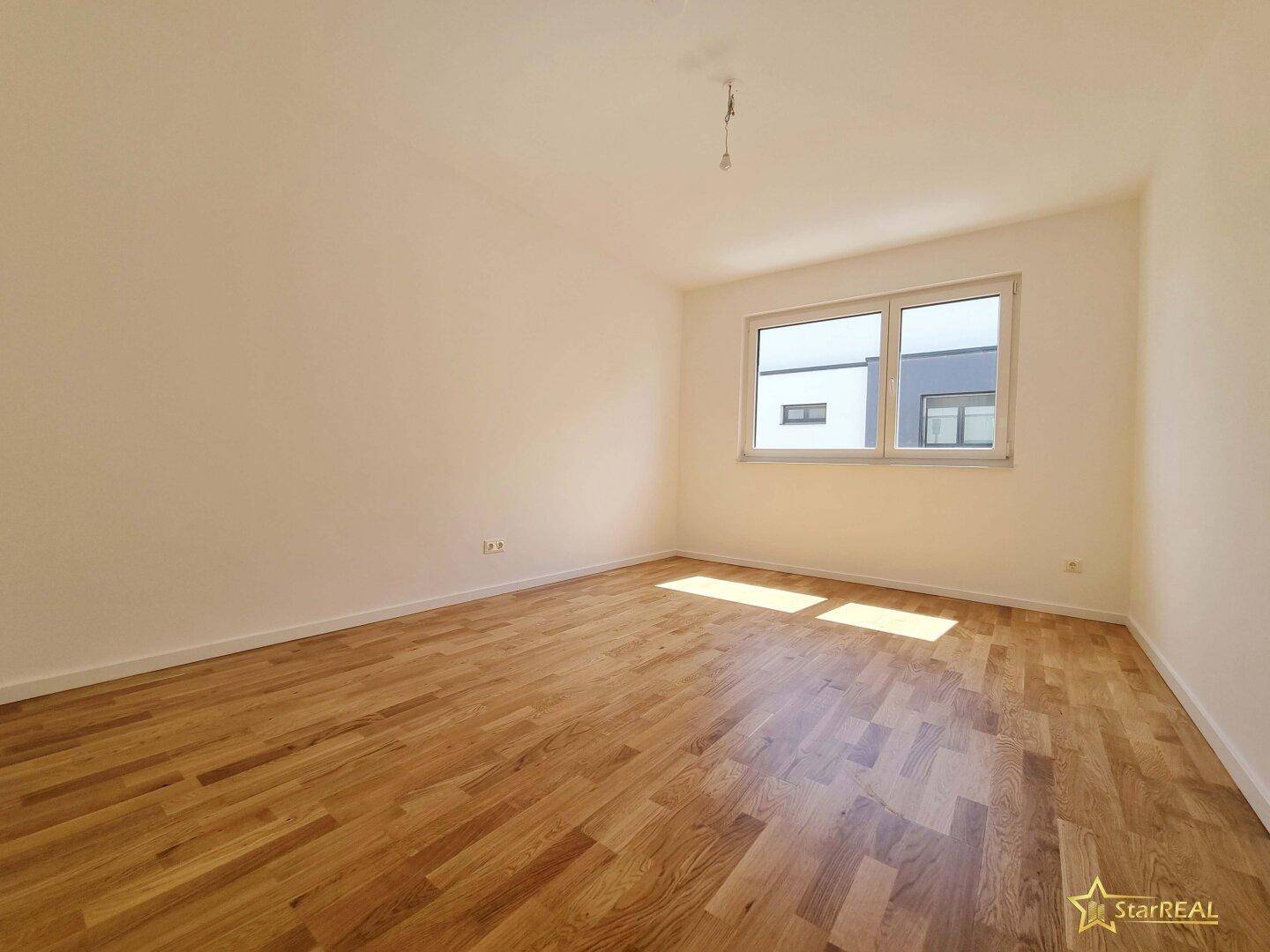Sonniges Schlafzimmer mit Parkettboden und einem großen Fenster.