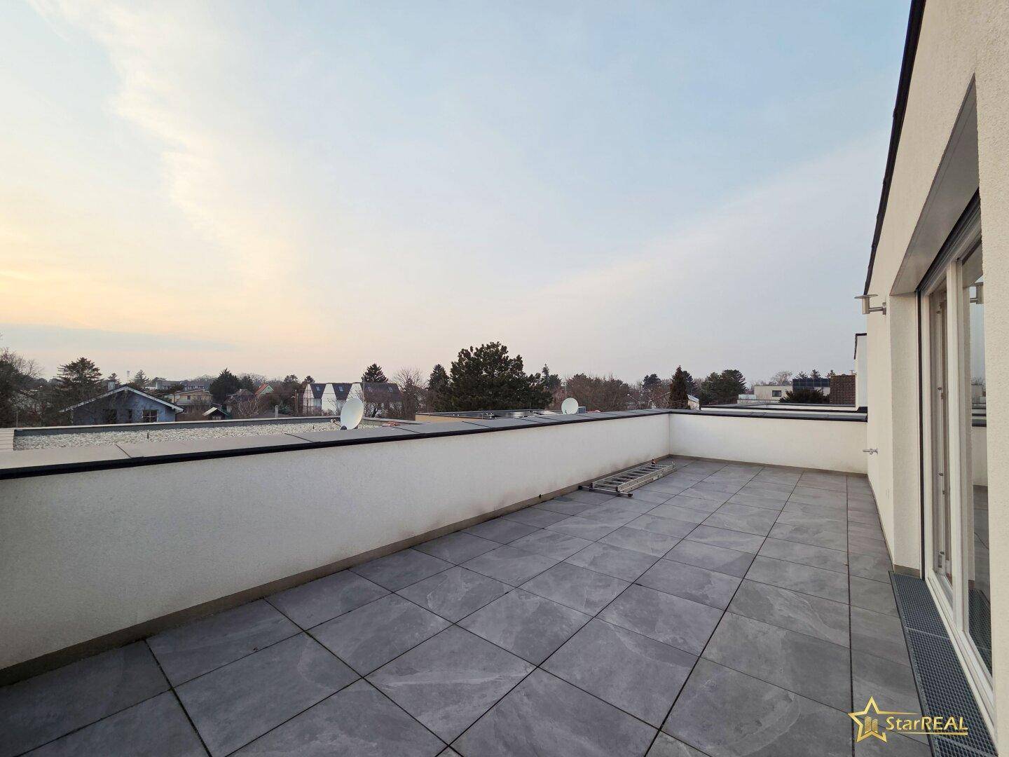 Geräumige Dachterrasse mit Fliesenboden und weitem Blick über die Umgebung bei Sonnenuntergang.