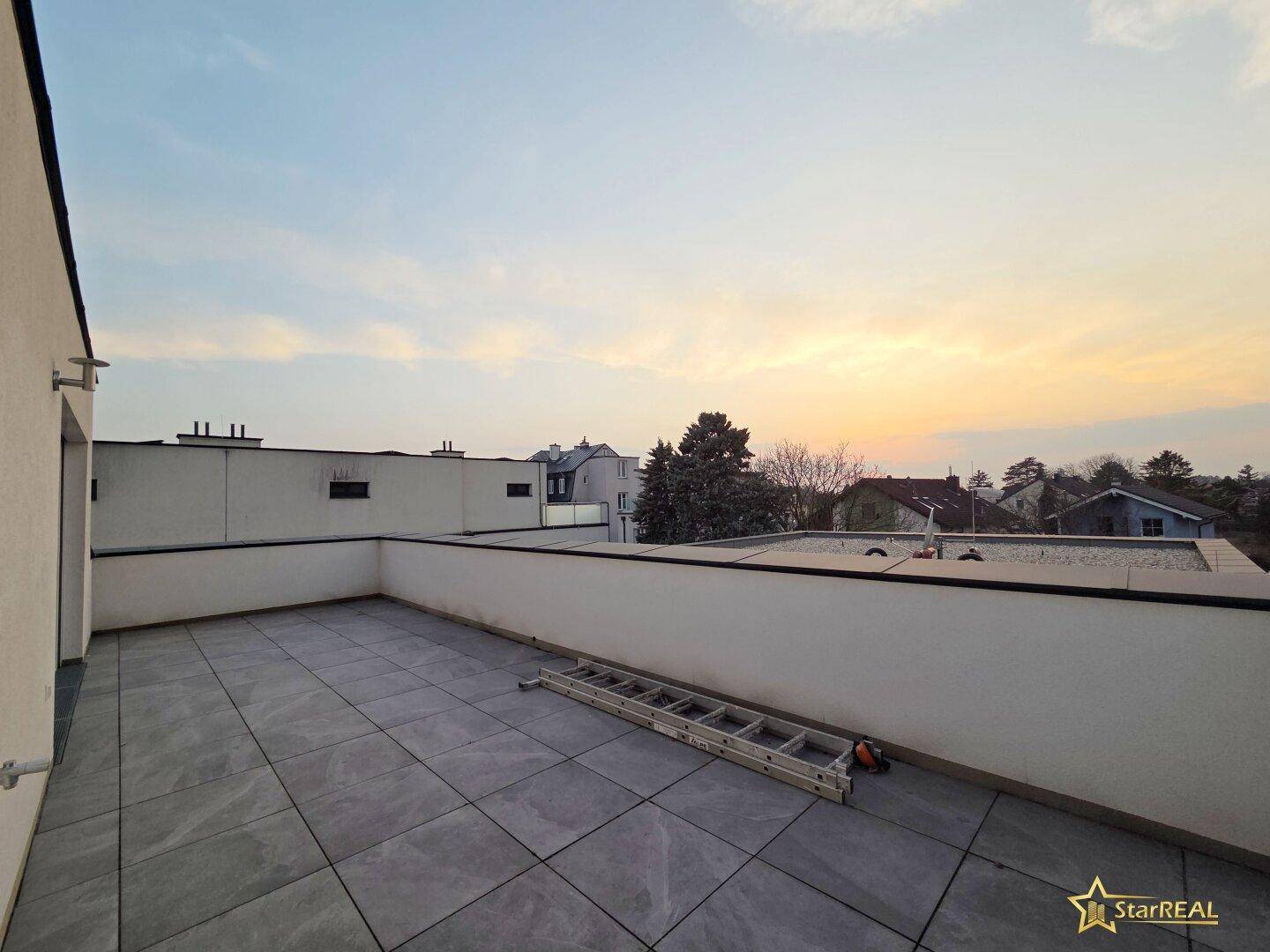 Weitläufige Dachterrasse mit Fliesenboden und Panoramablick in der Abenddämmerung.