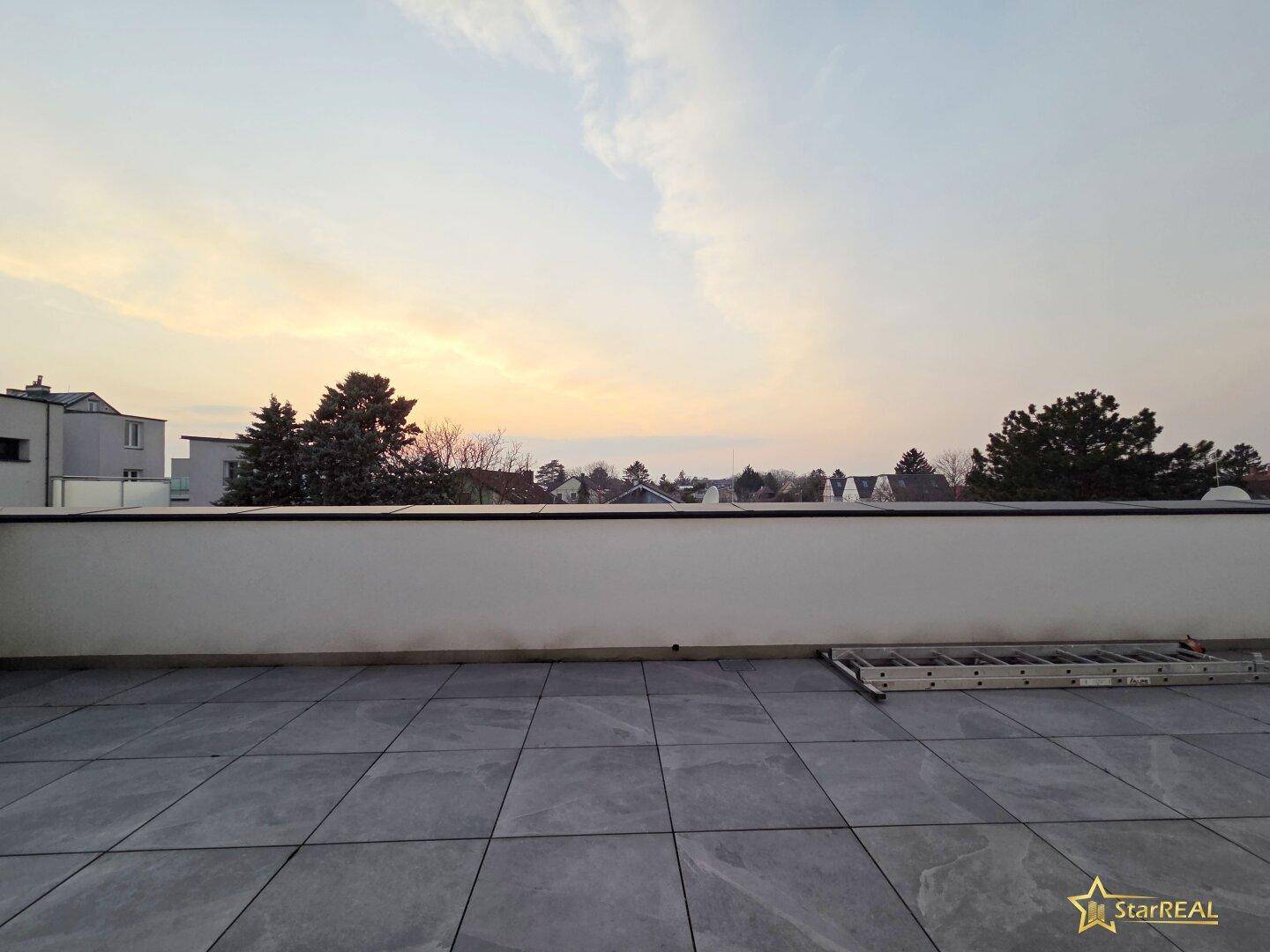 Große Dachterrasse mit Fliesen und weitem Blick über die Dächer bei Sonnenuntergang.