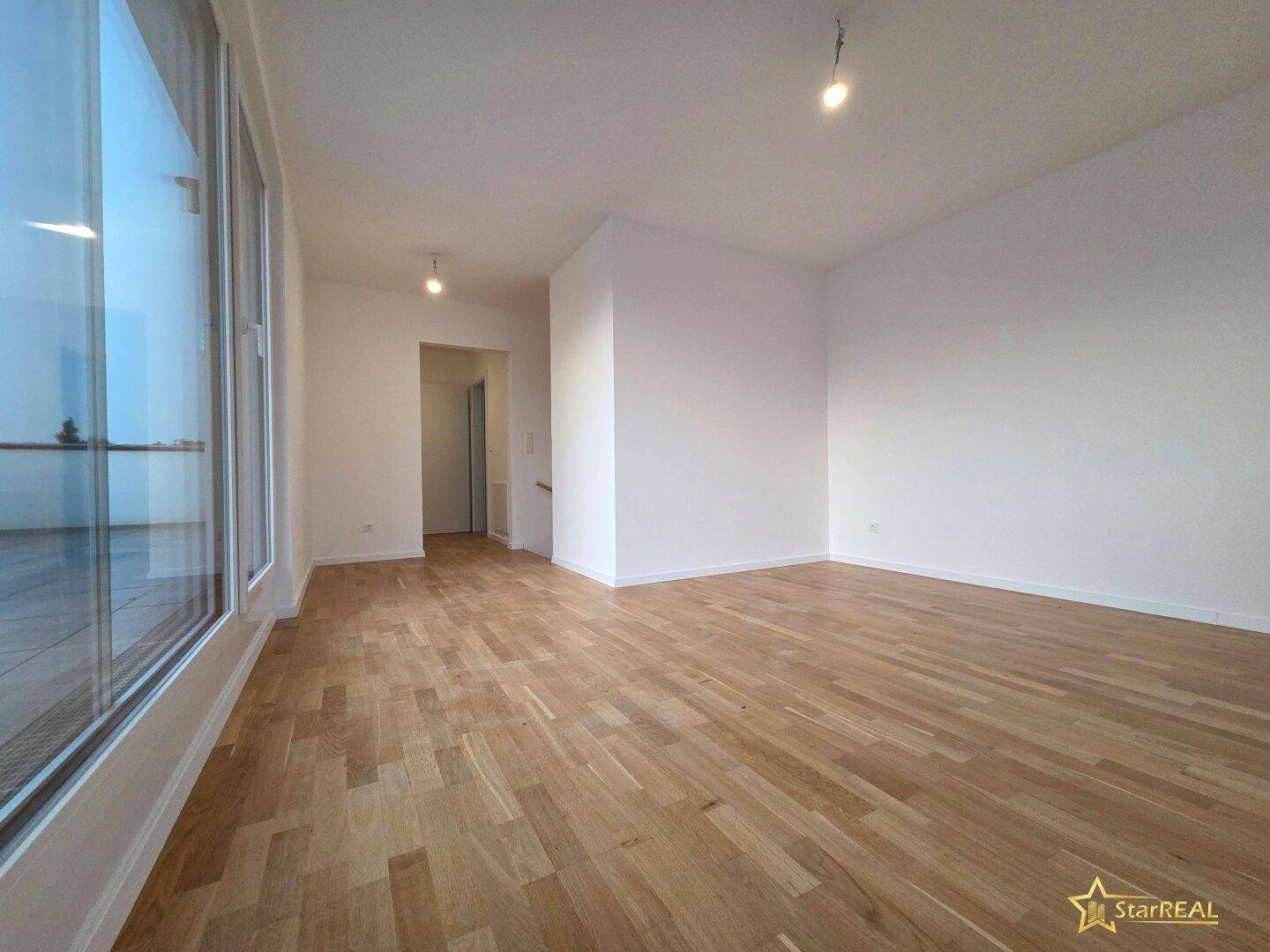 Heller Wohnraum mit Parkettboden und großen Fenstern mit Zugang zur Dachterrasse.