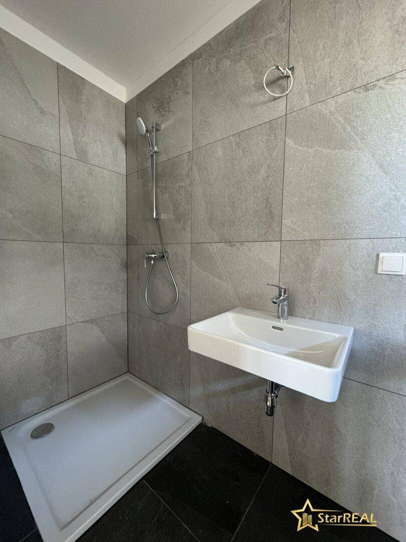 Modernes Badezimmer mit grauen Fliesen, einer Dusche und einem wandmontierten Waschbecken.