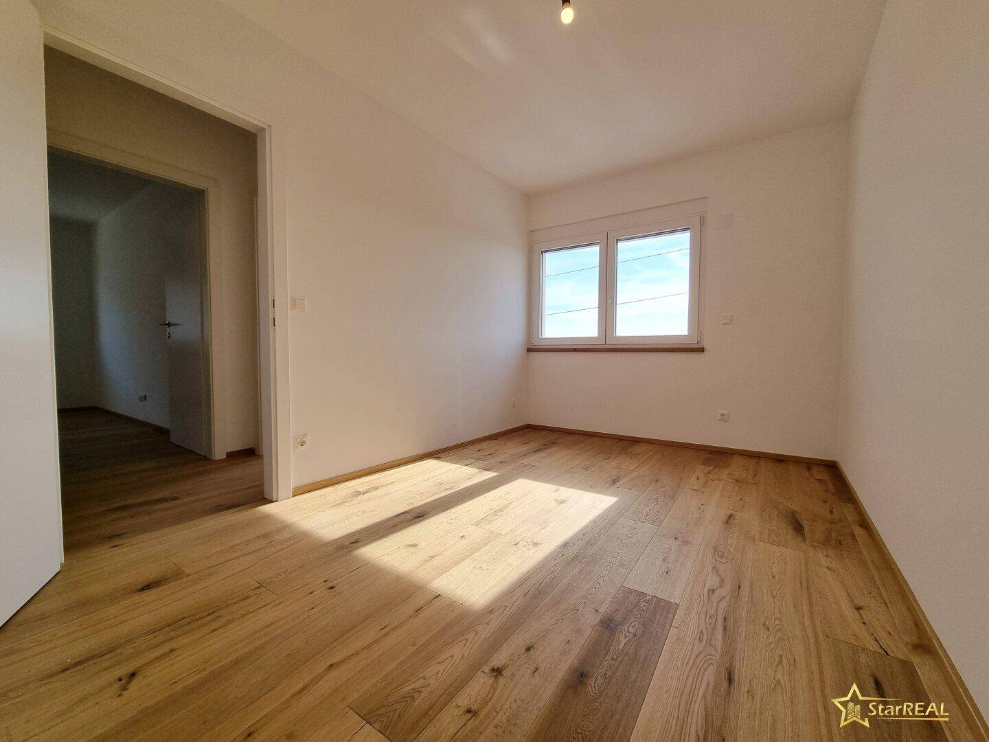 Helles Schlafzimmer mit Eichenparkettboden und einem Fenster, das viel Tageslicht bietet.