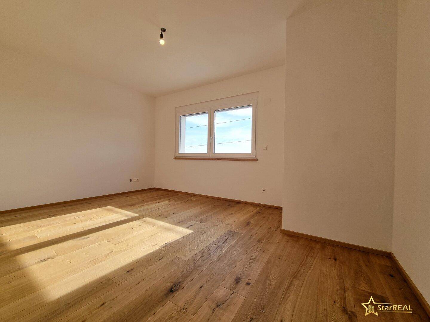 Helles Schlafzimmer mit Eichenparkettboden und einem Fenster, das viel Tageslicht bietet.