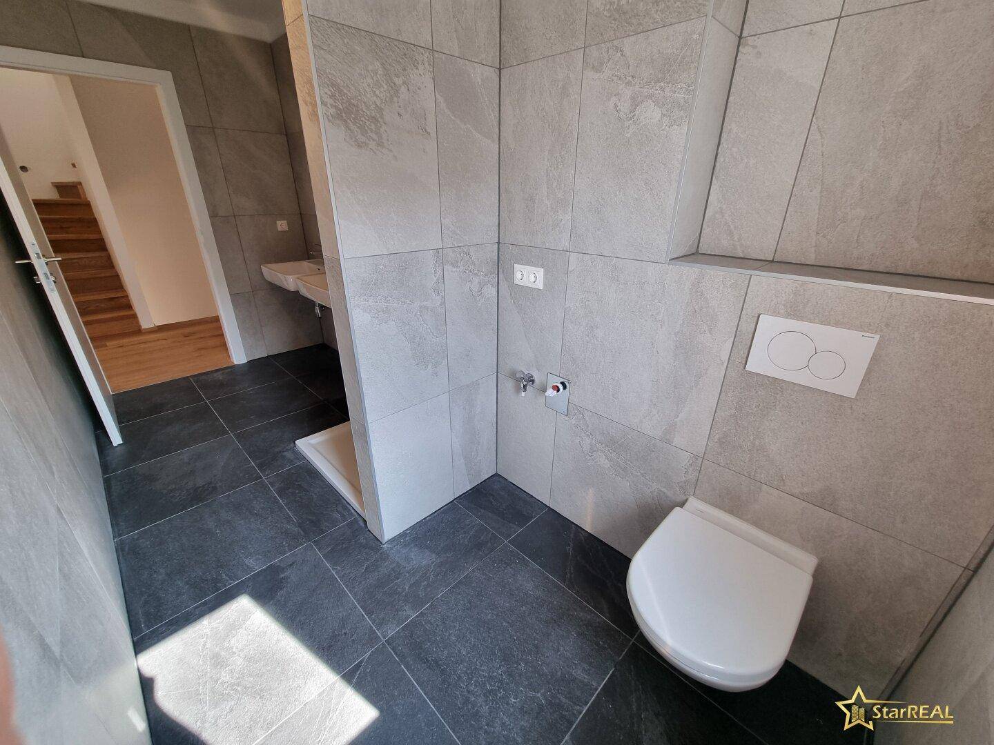 Modernes Badezimmer mit Wand-WC, Duschbereich und grauen Fliesen.