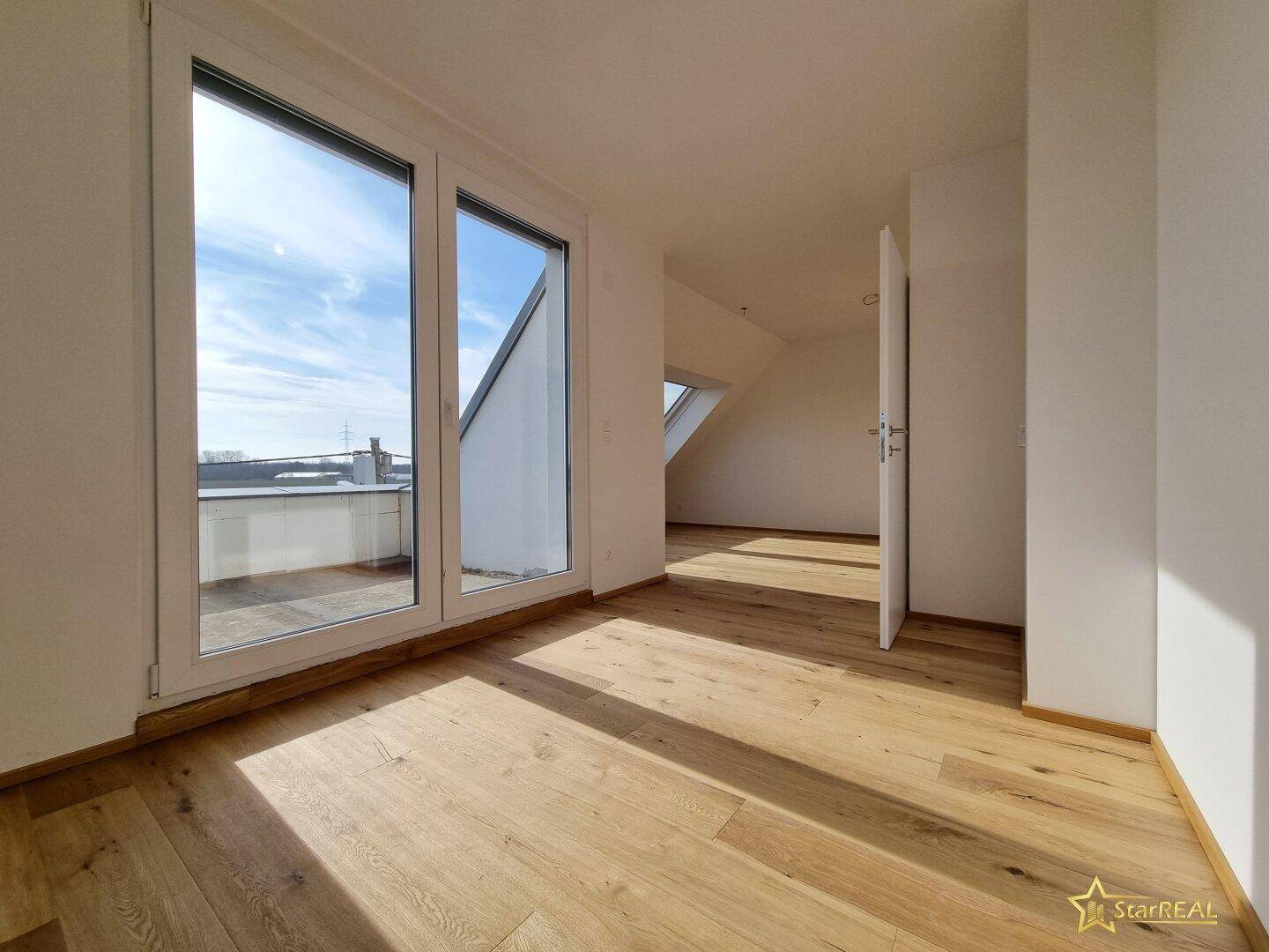 Lichtdurchfluteter Raum mit Holzboden und großen Glastüren, die Zugang zu einem Außenbereich bieten.