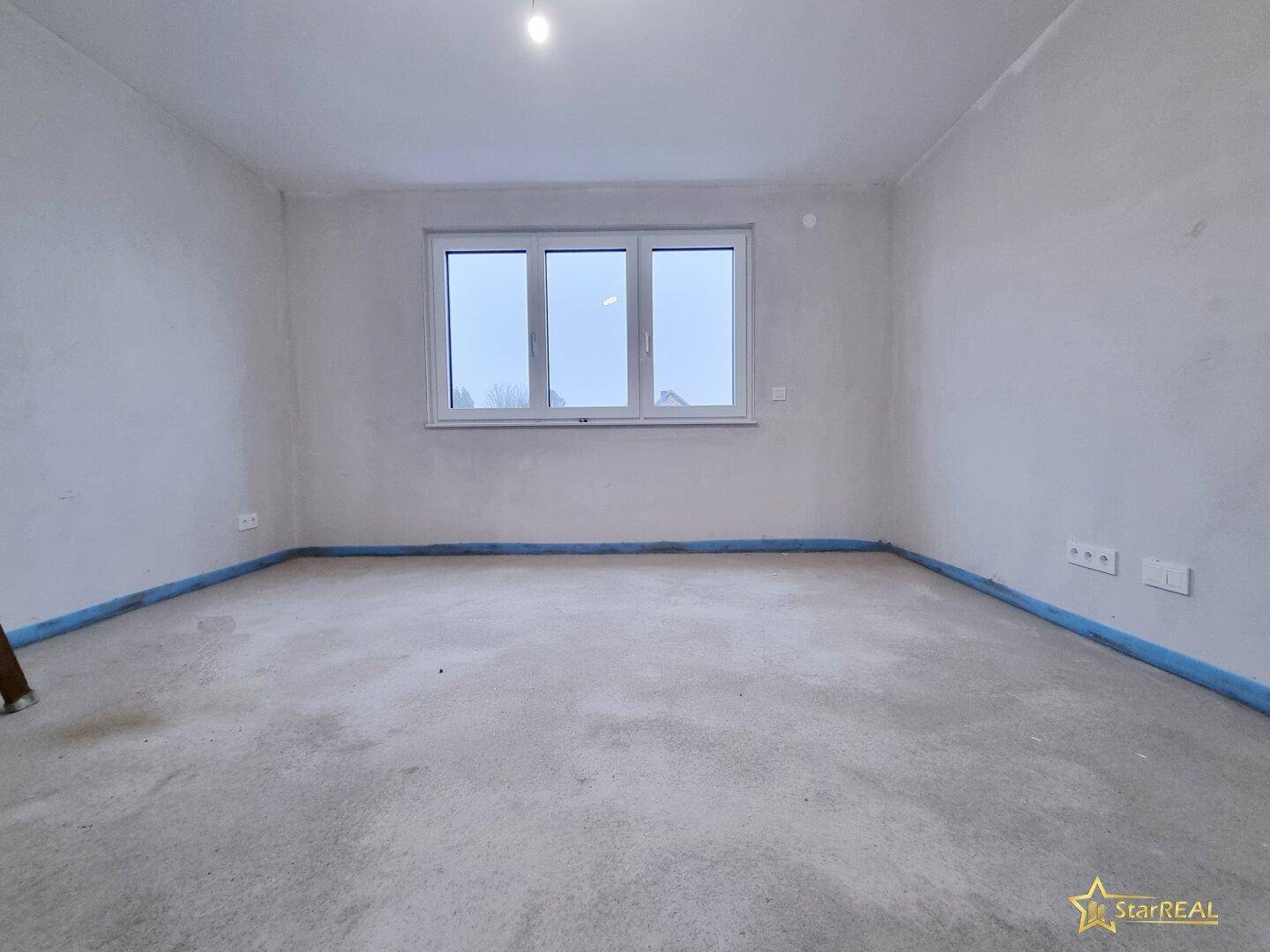 Heller Raum im Ausbauzustand mit großem Fenster und Betonboden.