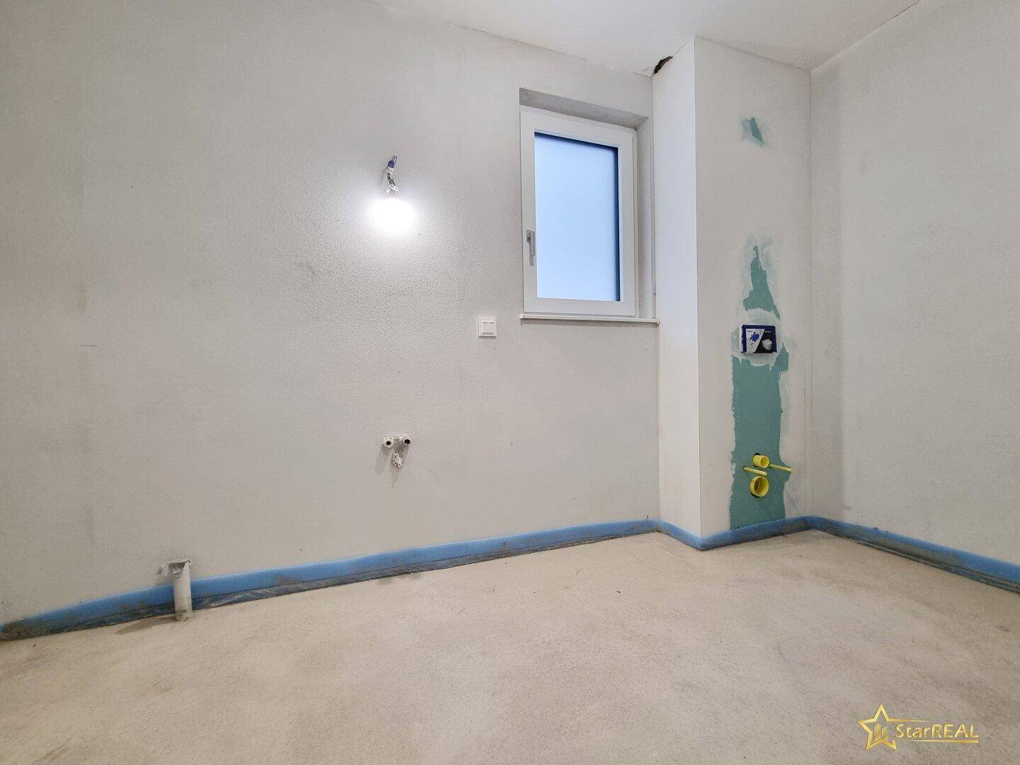 Badezimmer im Ausbauzustand mit vorbereiteten Anschlüssen und Fenster.