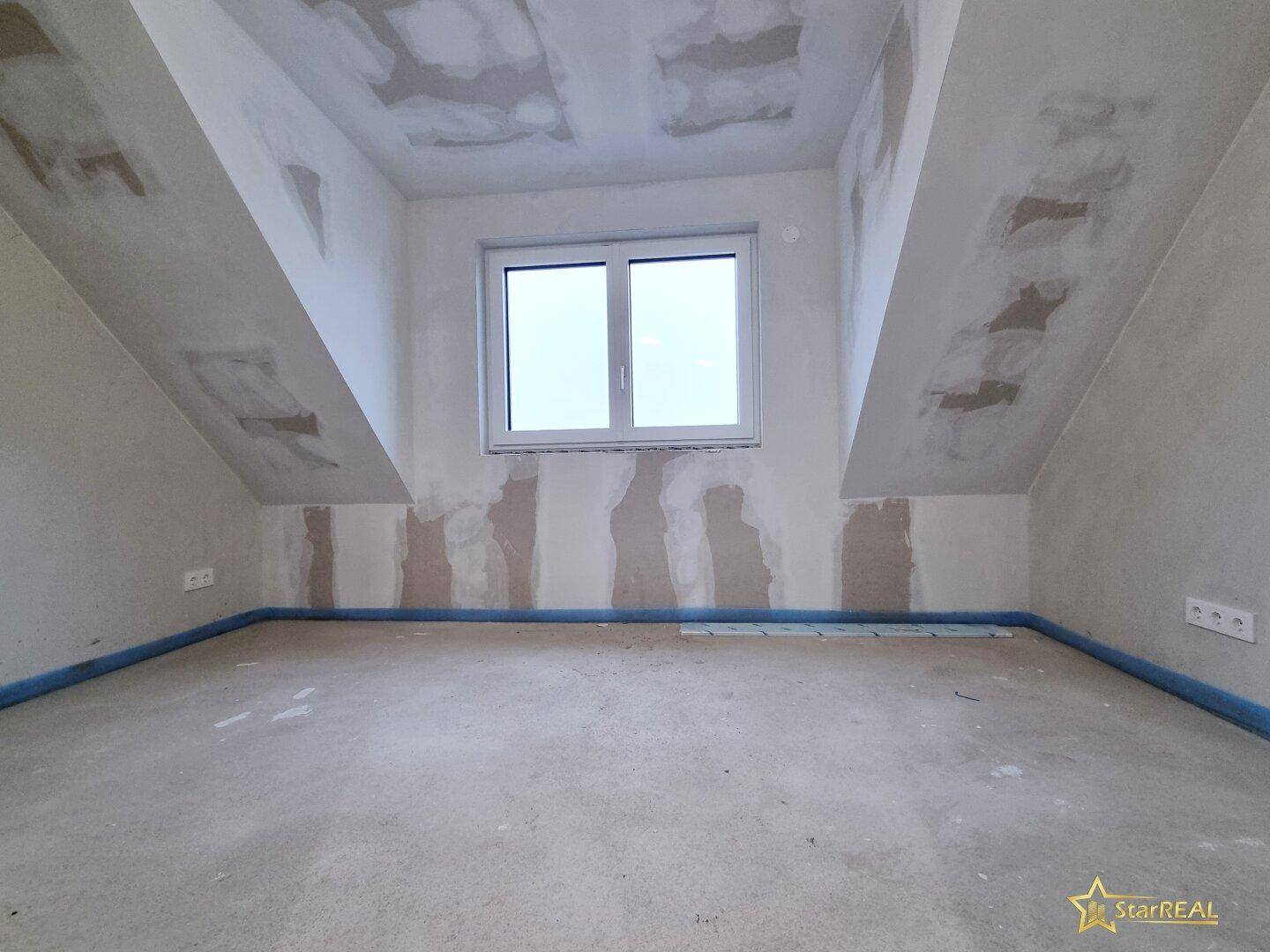 Dachgeschossraum im Ausbauzustand mit Gaubenfenster und schrägen Wänden.