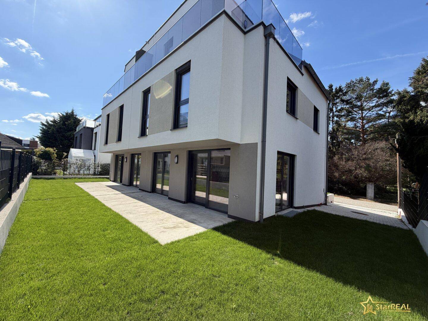 Moderne Neubaufassade mit gepflegtem Rasen und gepflastertem Weg unter blauem Himmel.