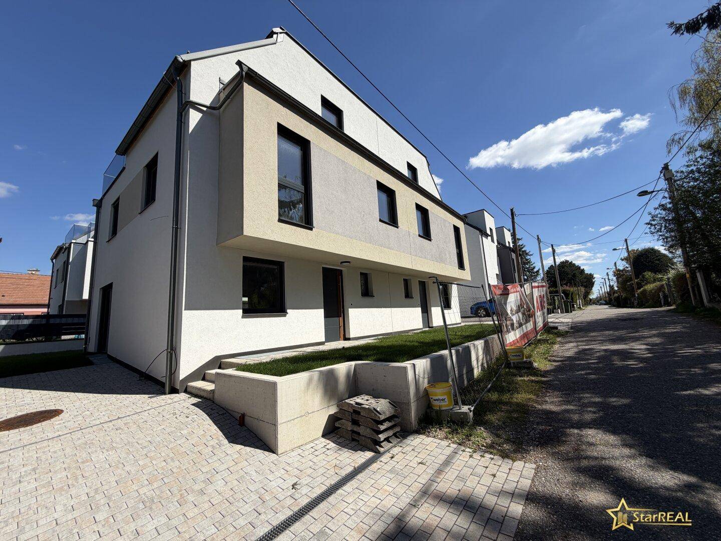 Seitenansicht eines modernen Neubaus mit heller Fassade und Zugangsbereich von der Straße.