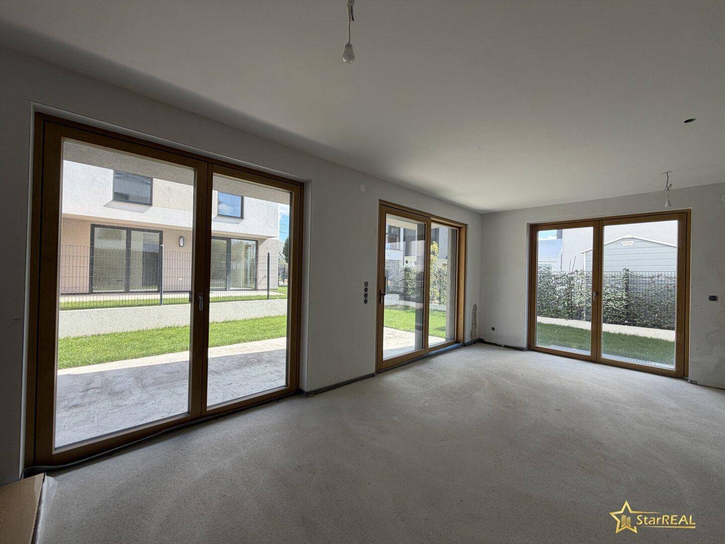 Heller, unfertiger Wohnbereich mit großen Fenstertüren und Blick auf den Garten.
