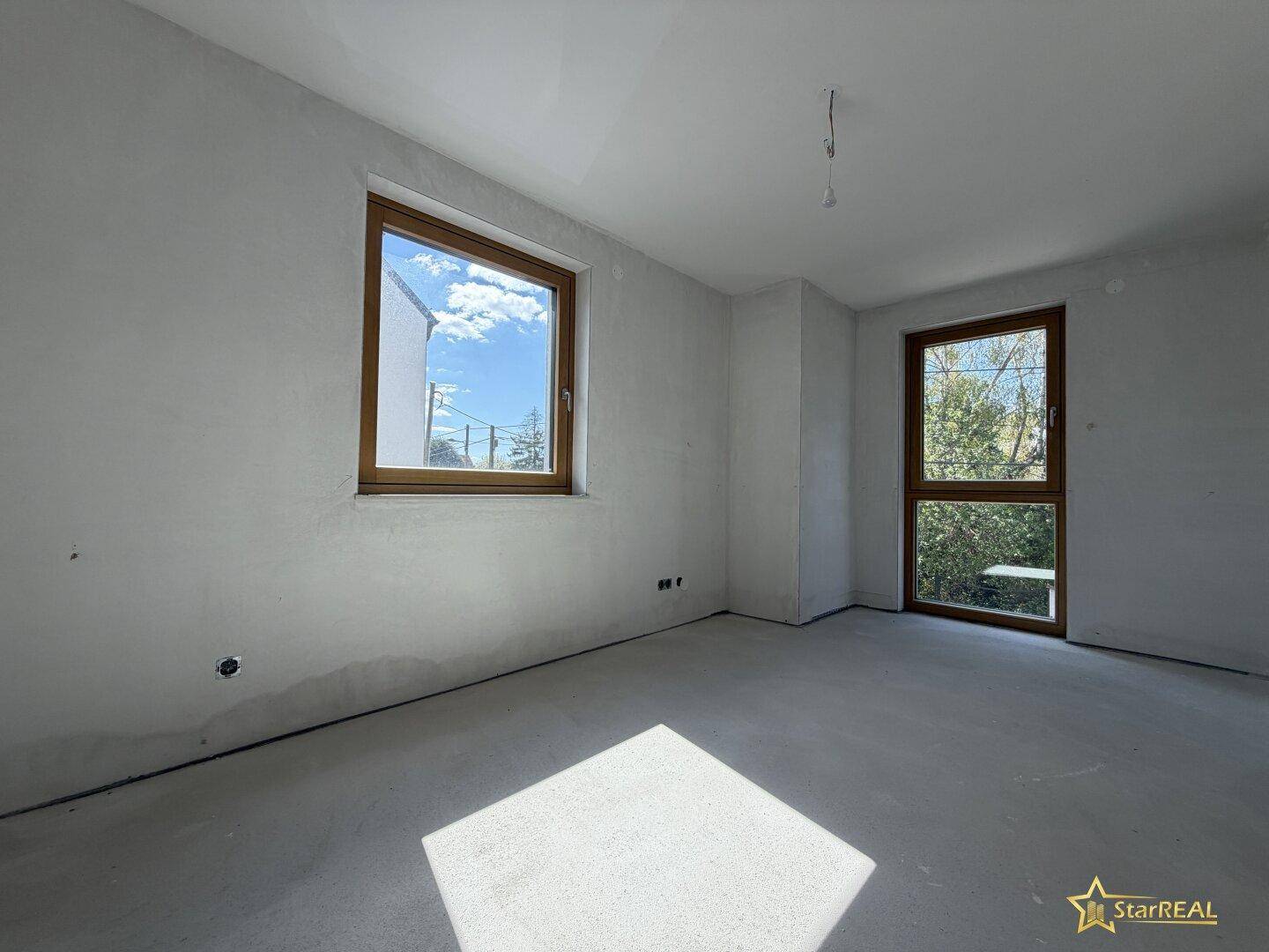 Heller, unfertiger Raum mit Fenster und Tür, bereit für den Innenausbau.