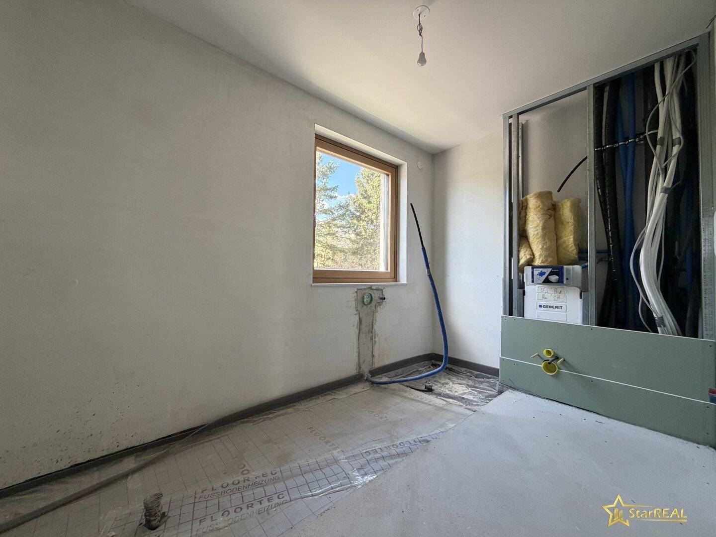 Unfertiges Badezimmer mit sichtbaren Installationen und Fenster für Tageslicht.