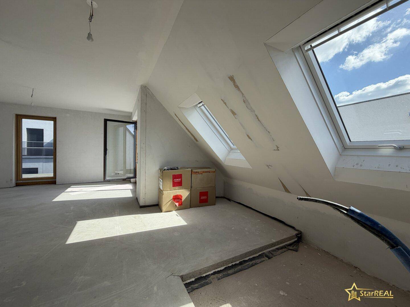 Heller Dachgeschossraum im Rohbau mit Dachfenstern und Zugang zur Terrasse.