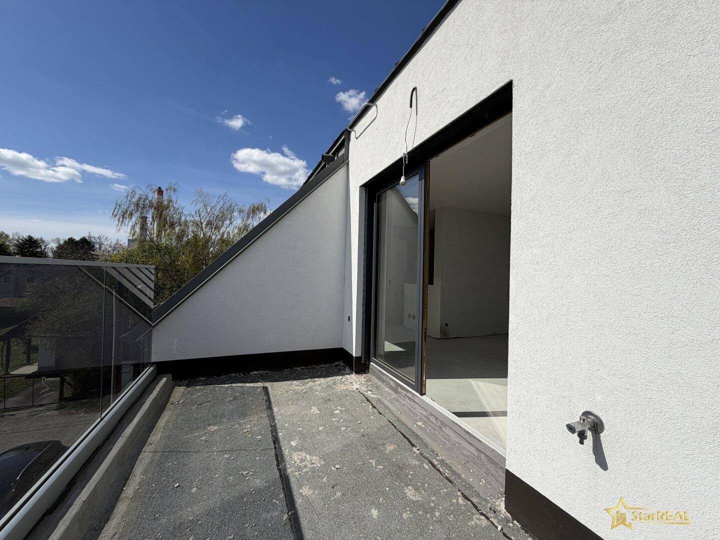 Dachterrasse im Bau mit Glasgeländer und Zugang zu einem Innenraum.